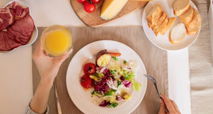 A top-view of a delicious breakfast setting featuring a salad, bread, cheese, tomatoes, and orange juice.