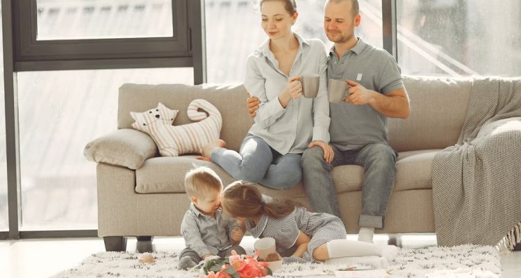 Cheerful family smiling while spending weekend together sitting parents sitting on comfortable sofa while children resting on carpet and playing